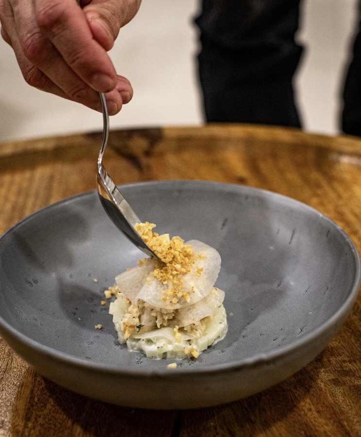 Chef finishing a plated starter with a golden crumble
