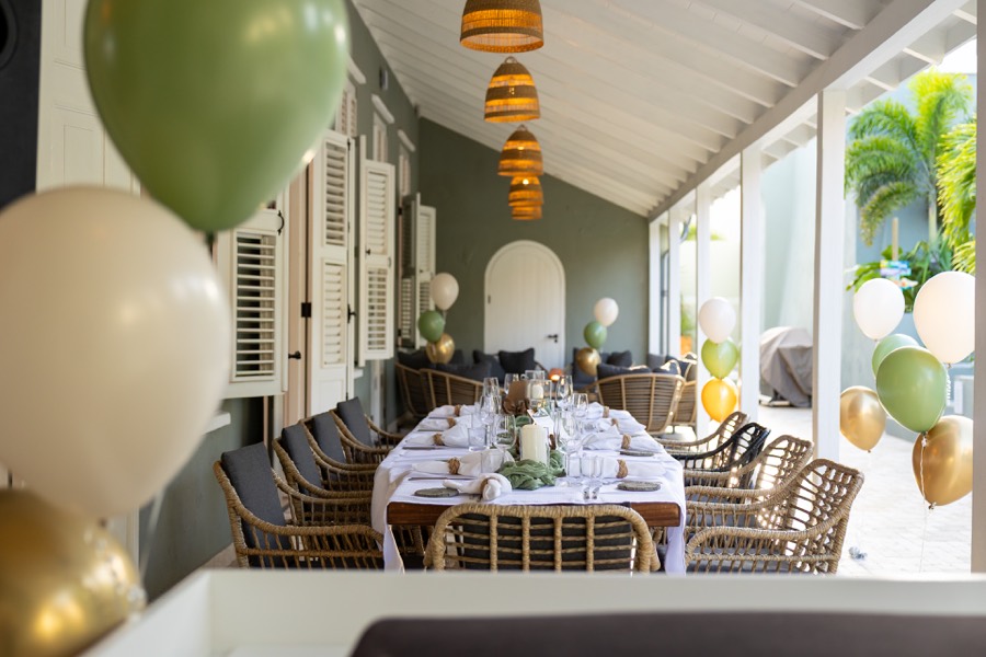 Long dinner table set on a covered veranda, decorated with balloons for a celebration