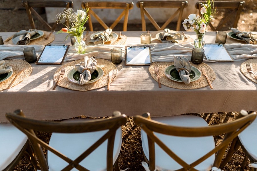 Long outdoor table set with linen, woven placemats, green plates and fresh flowers